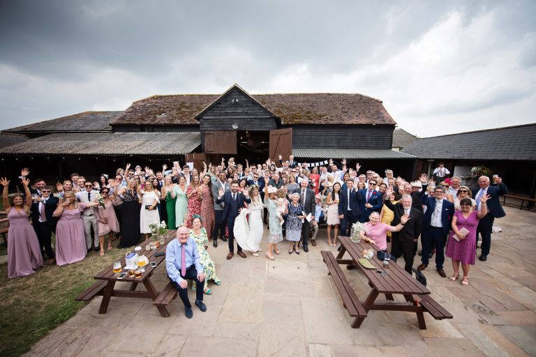 Large group photograph of everyone with their hands in the air like they don't care, smiling at Overbarn wedding venue.