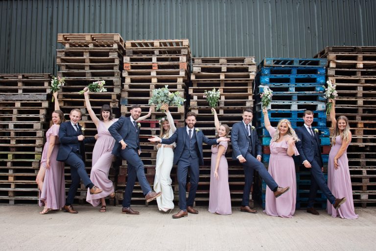 Bridal party striking poses next to wooden pallets. Looks fun.