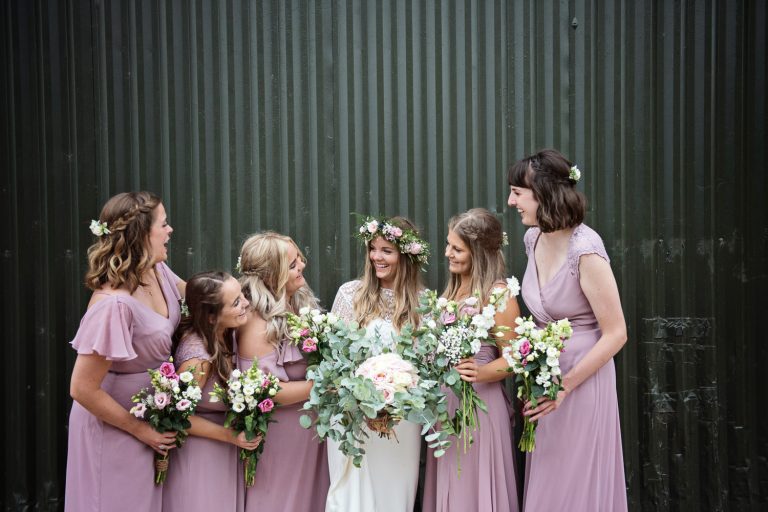 Bridesmaids and bride chatting with a green barn panel behind them.