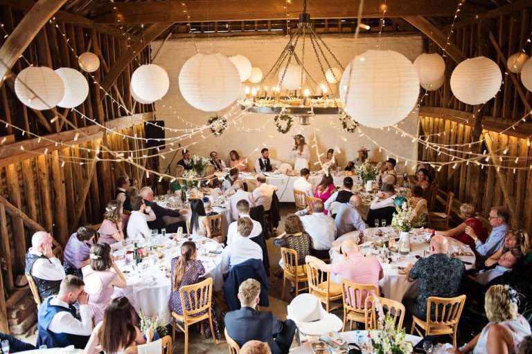 Wedding breakfast in full swing (lots of people sitting around decorated wooden wedding tables) in Overbarn.