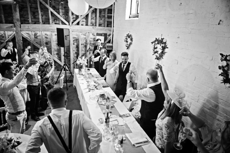 B&W image of a wedding party cheering at the end of the speeches.