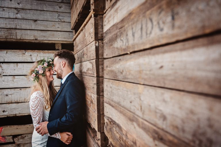 Bride and groom kiss next to a wooden panel part of a wedding barn.