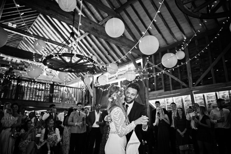 Bride and groom do their first dance with all their friends and family watching. B&W image.