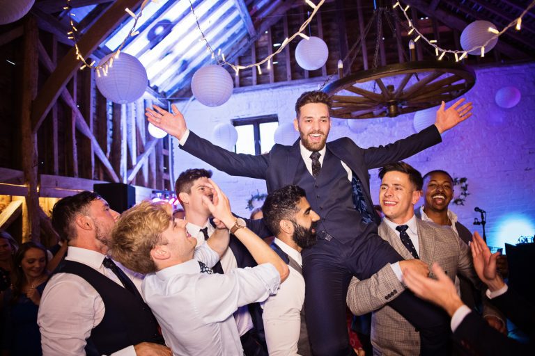 A groom being picked up in the air by his friends during his wedding party.