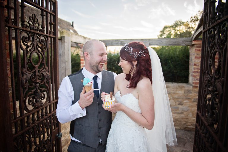 Bride and groom standing relaxed and smiling naturally as they eat ice cream.