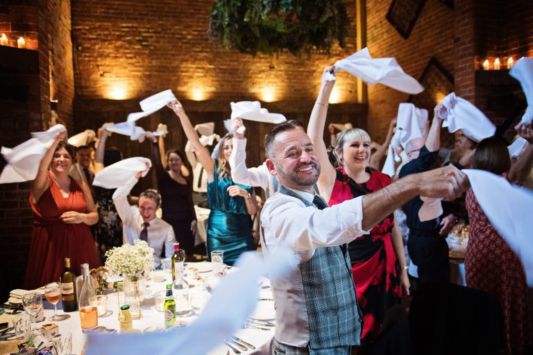 Candid photo of wedding guests celebrating the entrance of the bride and groom with spinning their napkins in the air.