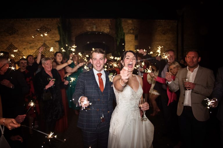 Bride and groom and wedding guests holding sparklers up in the air.