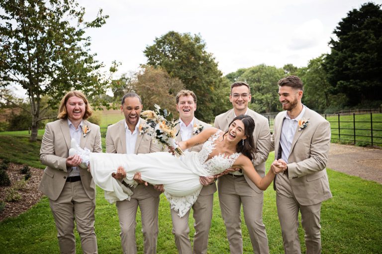 Bride being held up (just), by the groom and groomsmen. Bride is laughing.