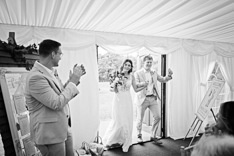 B&W photo of bride and groom being announced into the marquee at Slapton Manar.