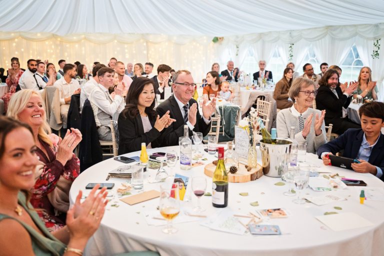 Candid photo of wedding guests clapping in a marquee.