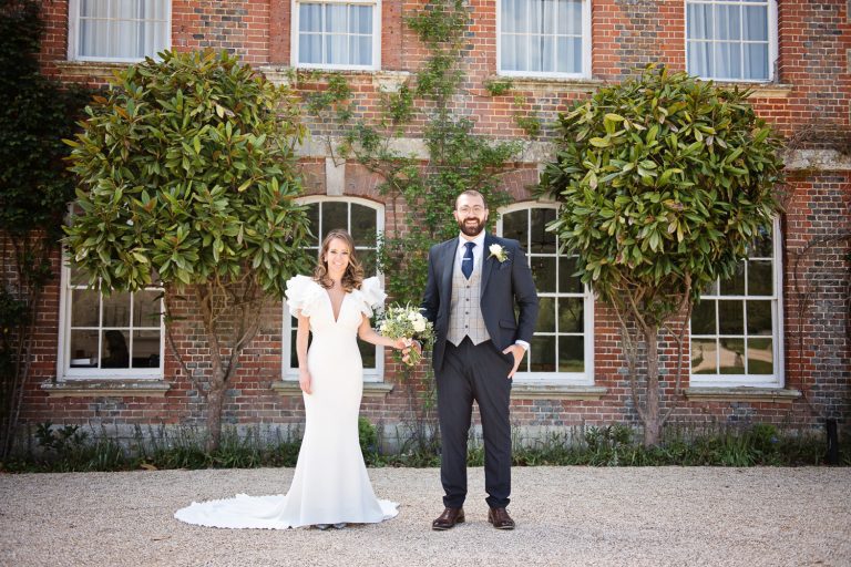Bride and groom stand in front of Syrencot House, both smiling and relaxed.