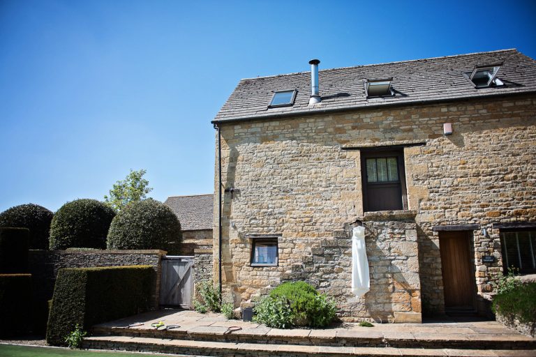 Wedding dress hung up on the steps of a Cotswold Barn.