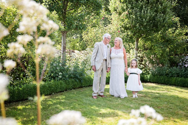 Bride and her father and flower girl stand in the garden.