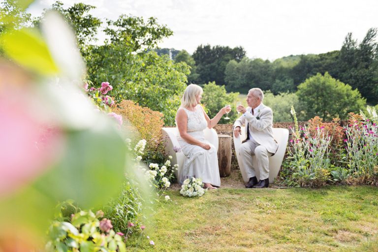 Bride and groom share a moment together sitting down in a luxurious garden setting.