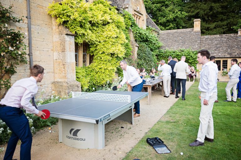 Wedding guests relaxing playing table tennis in the gardens of a Cotswold venue.