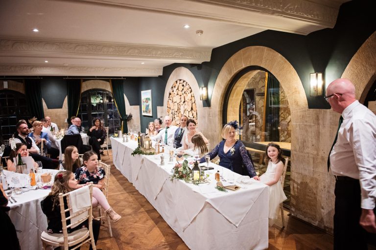 Candid photo of the father of the bride delivering his speech with the bride and rest of the guests looking onwards.