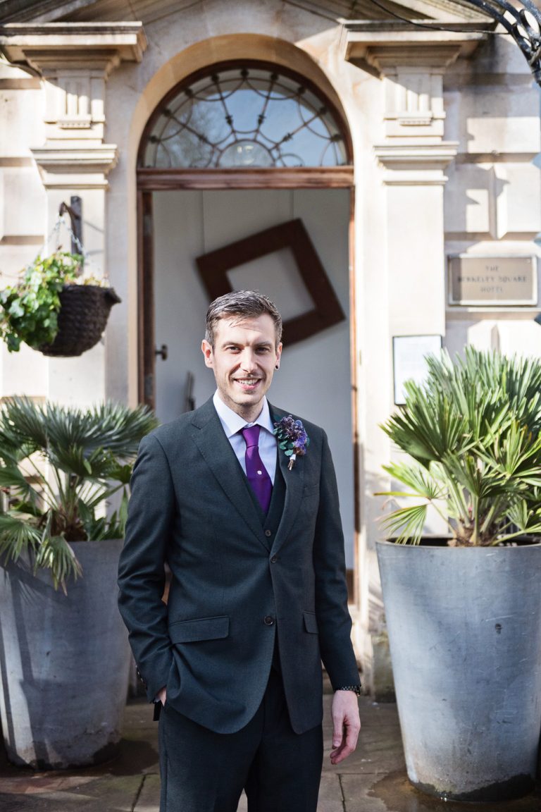 Portrait photo of the groom. Tall plant pots to either side of him.