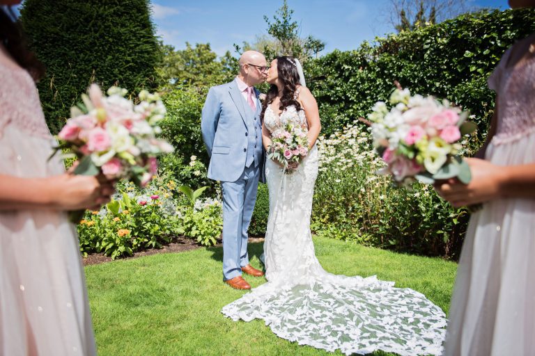 Bride and groom kiss with bridesmaids standing in front framing the picture.
