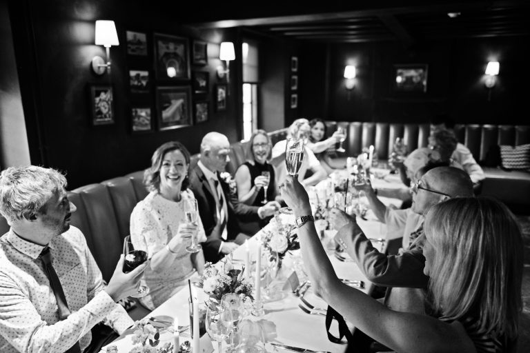 Fun B&W photo of wedding guests cheering each other with their wine glasses.
