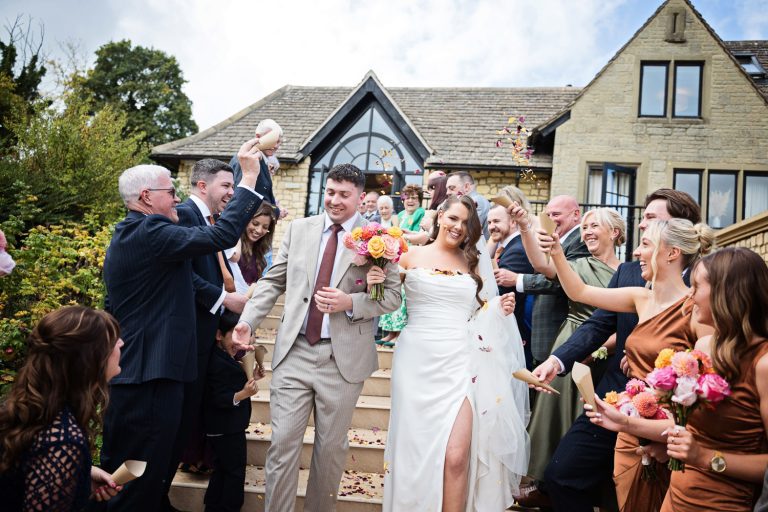 Candid photo of Bride and groom walking down the steps as their wedding guests throw confetti over them.