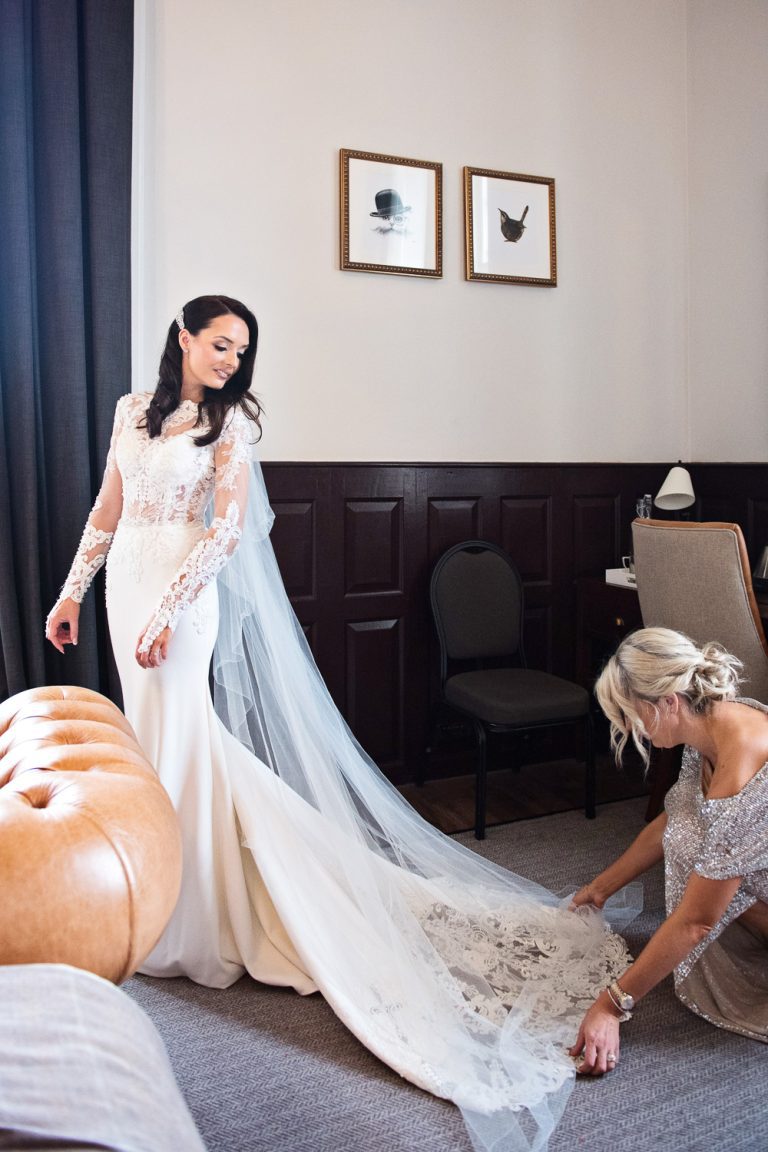Portrait photo of the bride in her wedding dress. Bridesmaid layign the veil out.