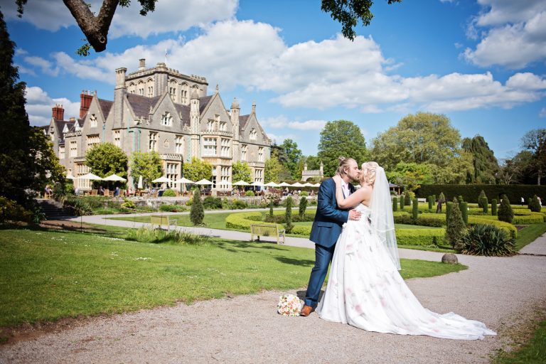 Bride and groom kissing but with Tortworth Court and formal gardens behind them.