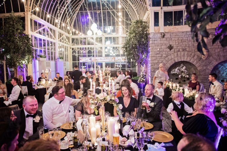 Atmospheric evening time shot of the Orangery lit up. Wedding guests enjoying themselves. Candid. Storytelling photo.