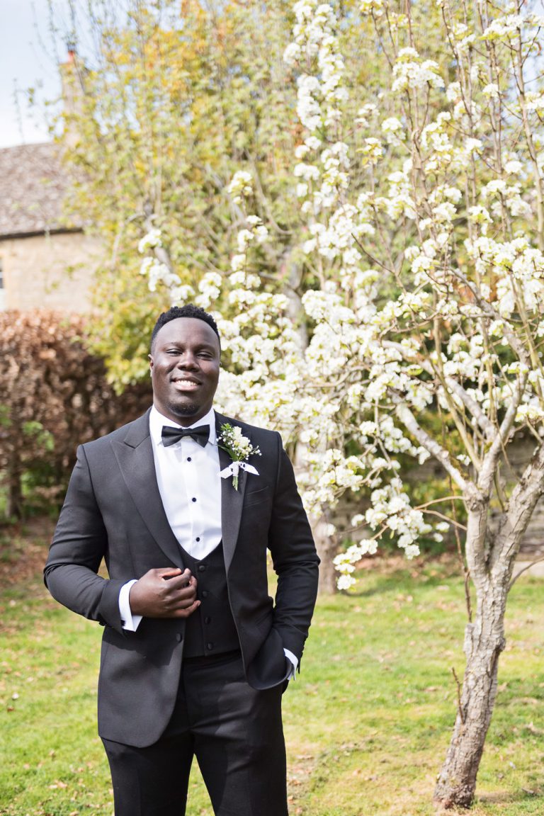 Portrait photo of groom standing beside a tree in blossom.