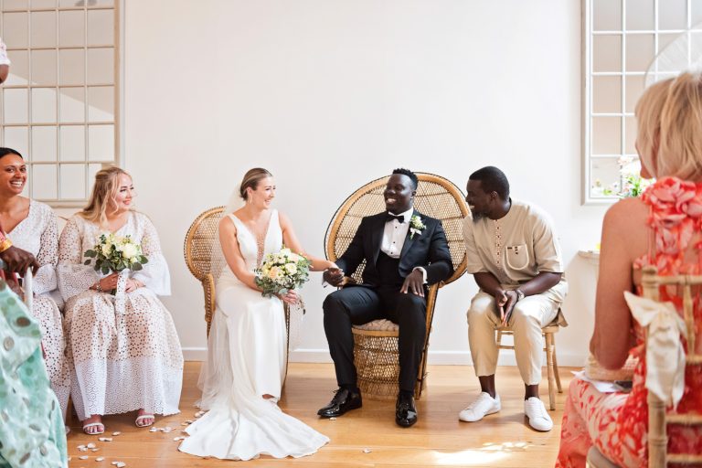Bride and groom sit and hold hands as they are having their wedding ceremony.