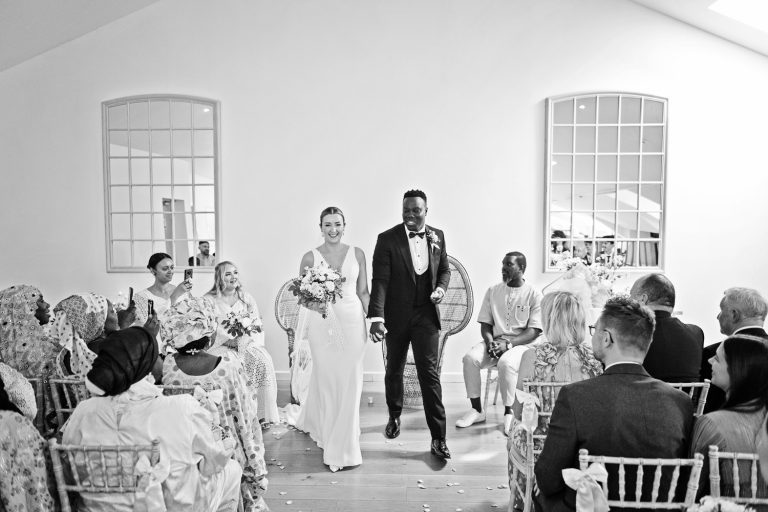 B&W candid photo of bride and groom walking down the wedding isle at Worton Hall.