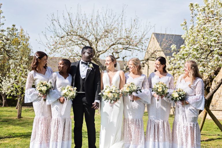 Bridesmaid and bride and groom stand in front of blossoming tree's at Worton Hall.