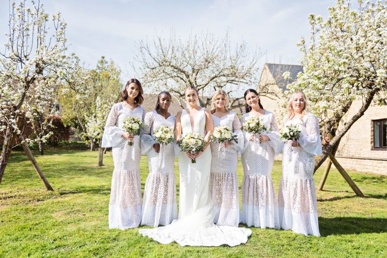 Bridesmaids standing on the lawn in front of flowering trees.