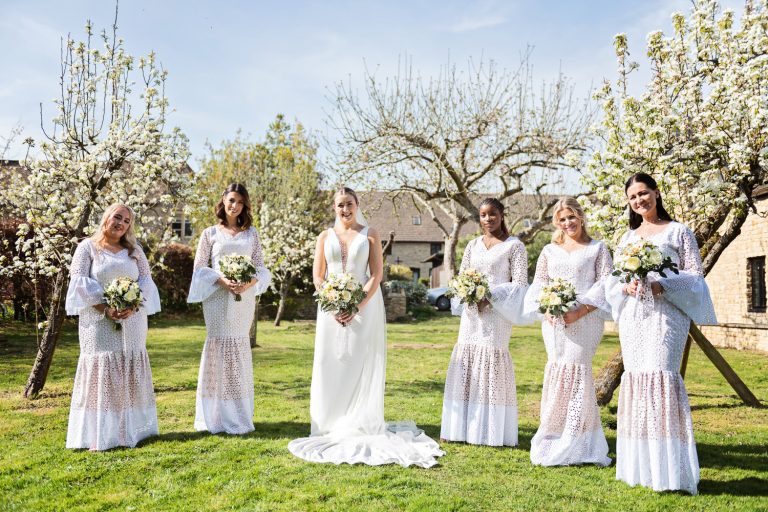 Bridesmaids standing on the lawn in front of flowering trees.