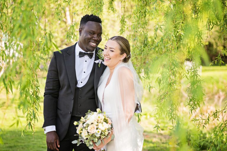 Bride and groom stand underneath a willow tree. Relaxed.