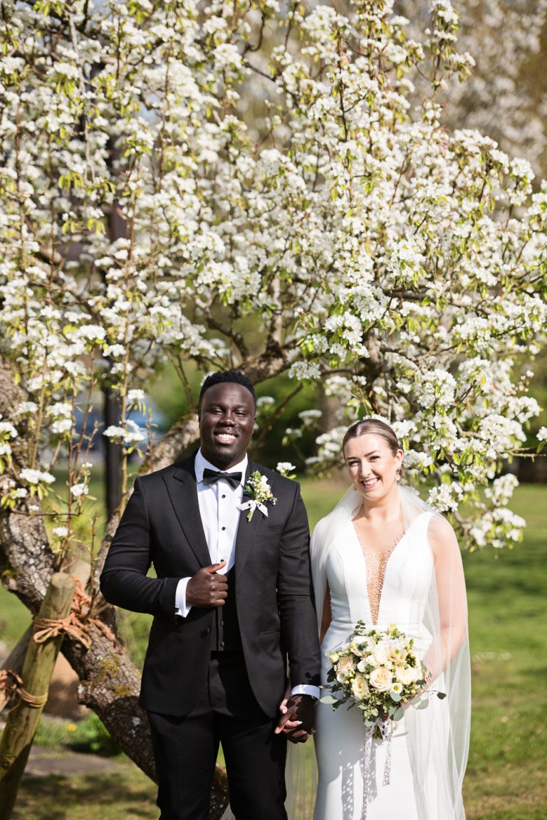 Bride and groom looking cool in front of a blossoming fruit tree.