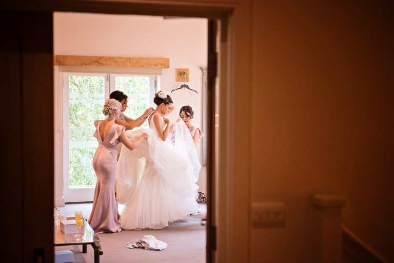 Looking through the door seeing the bride getting ready in her wedding dress, candid pic.