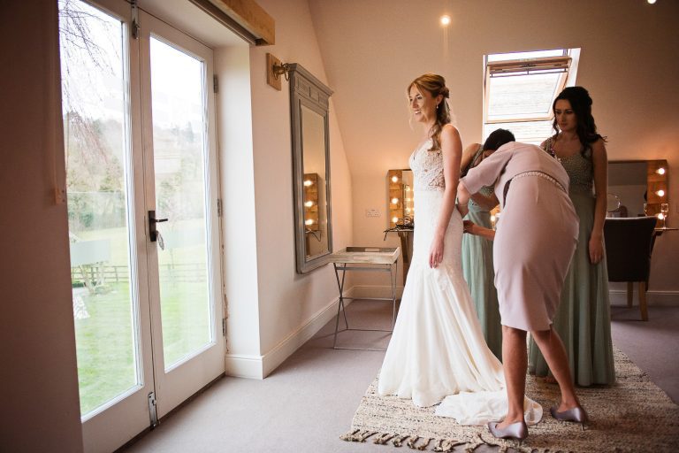 Candid photo of bride in her wedding dress being helped by her bridesmaids.