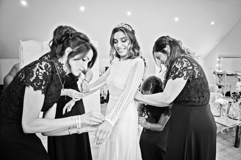 B&W photo of bride in her wedding dress being helped by her bridesmaids at Hyde House.