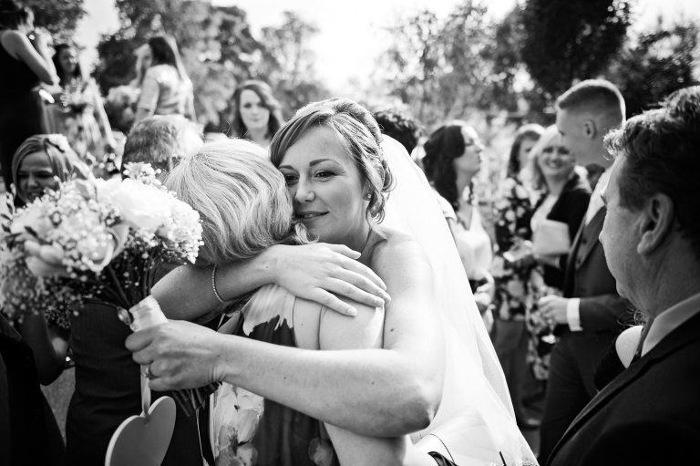B&W Candid photo of bride and groom getting congratulated by their wedding guests.