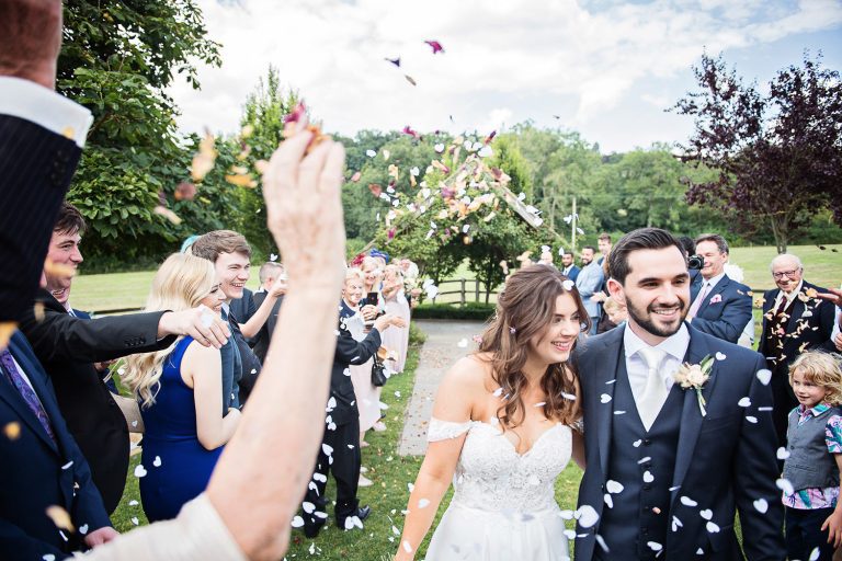 Photo of bride and groom getting showered with confetti by their guests.