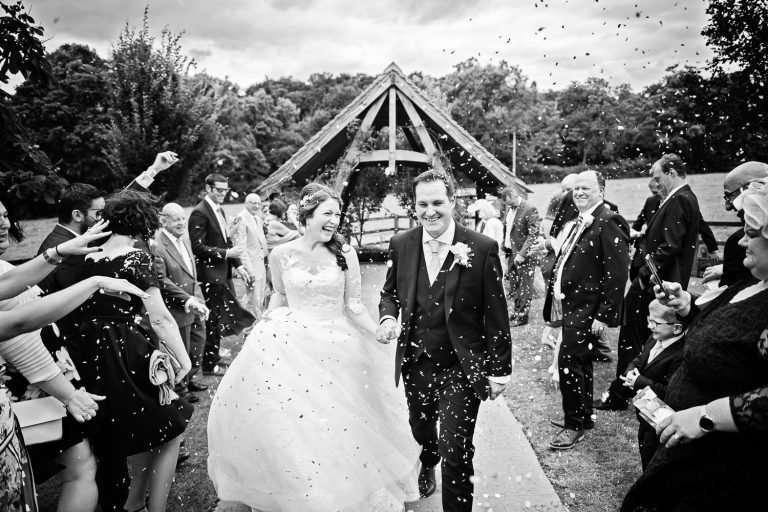 B&w photo of bride and groom getting showered with confetti by their guests.