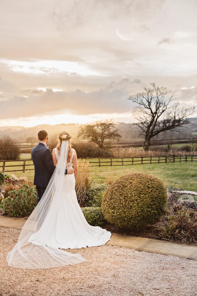 Bride and groom walk hand in hand at sunset.