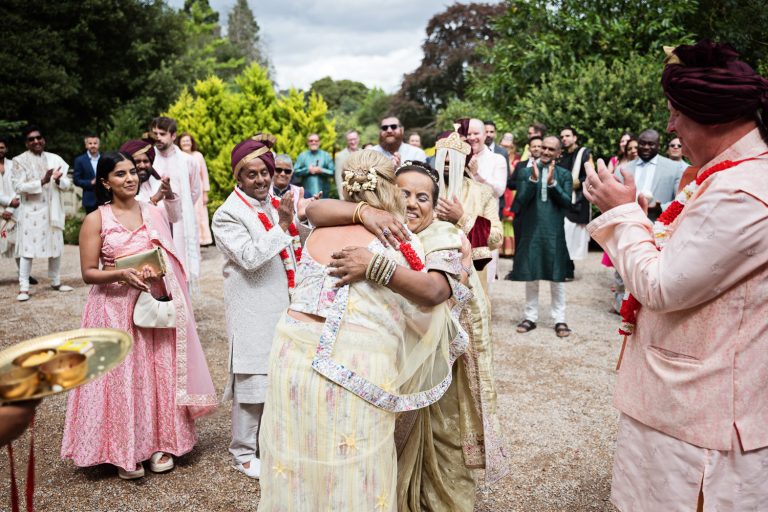 Storytelling candid photo of mother of the bride and mother of the groom hugging during the Baraat. Everyone else clapping and smiling.