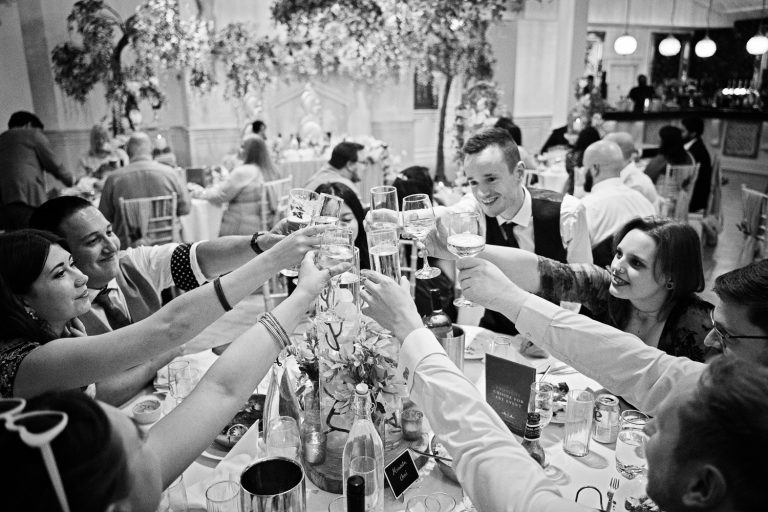B&W photo of guests celebrating by putting their glasses together and cheering.