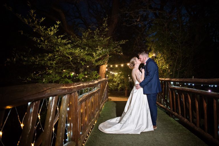 Night time photo of bride and groom kissing on the bridge at Manor By The Lake