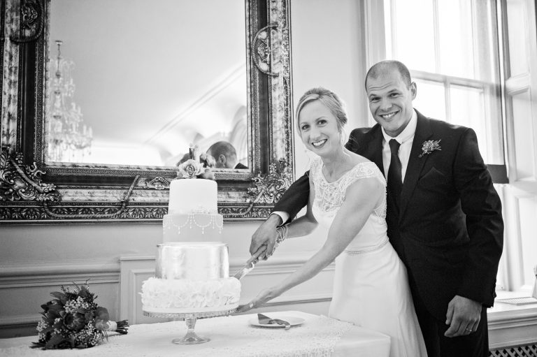 B&W candid photo of the bride and groom cutting the cake.