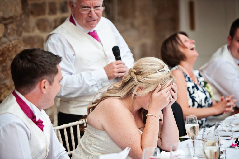 Candid photo of bride holding her head in her hands during speeches at Ellenborough Park.