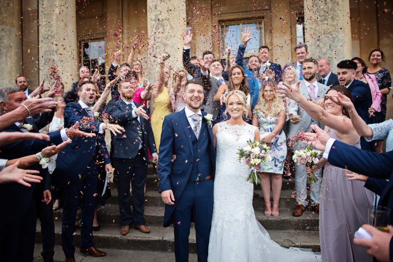 Bride and groom get showered by confetti by their guests on the steps at Pittville Pump Rooms.