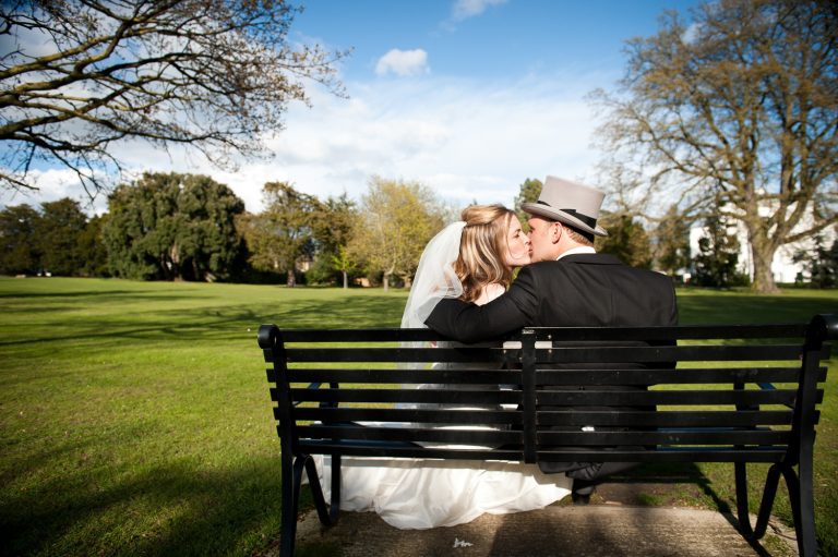 Bride and groom take a moment together as they kiss on a park bench in Pittville Park.