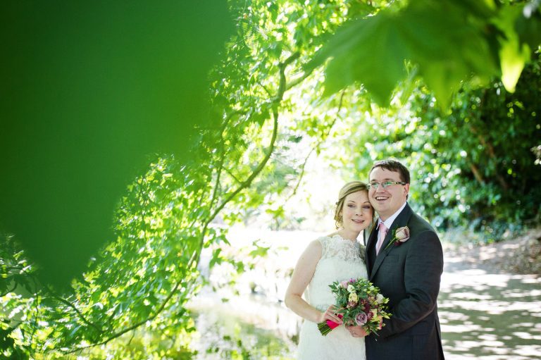 Bride and groom grab a moment together under the tree, by the lake in Pittville Gardens.